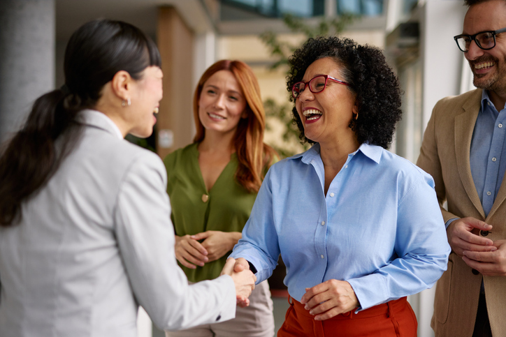 A group of diverse business colleagues engaged in a friendly handshake in a modern office setting, symbolizing partnership and cooperation. The atmosphere is positive and professional.