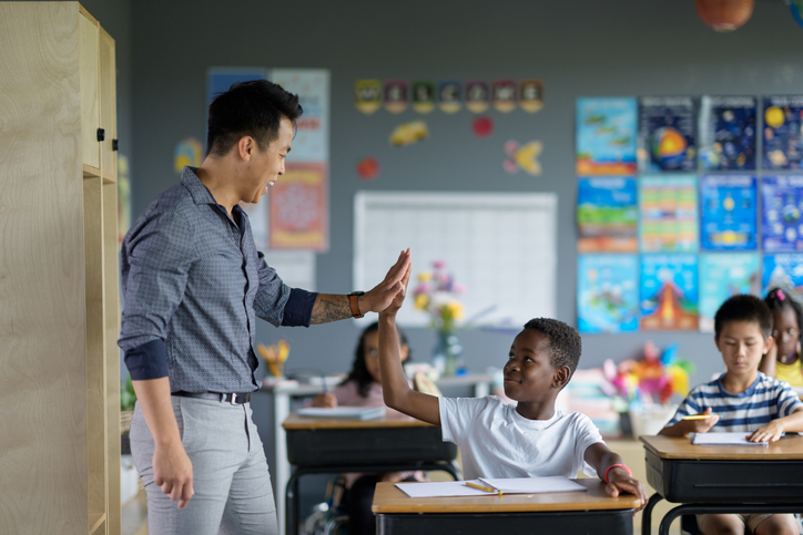 A teacher engages with a diverse group of students in a colorful classroom, emphasizing encouragement and teamwork.